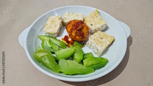 Photos Steamed tempeh, boiled small chayote and eggs with balado chili sauce, served on a white plate, food for dieters