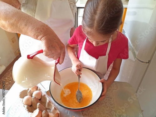 A grandmother and her granddaughter are making pancakes in the kitchen