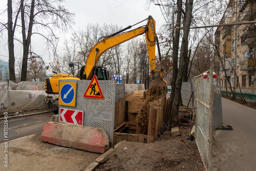 Reconstruction of the underground sewer system on a city street in winter. An excavator digs a deep trench. Traffic on the section of the street is stopped. Road works.