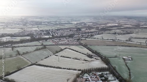 Aerial drone footage pushing forward over Willington village in Derbyshire, England, showing roads and snow covered fields for travel, rural infrastructure and establishing shot use.