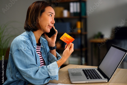 Worried Asian woman holding credit card and using laptop at desk