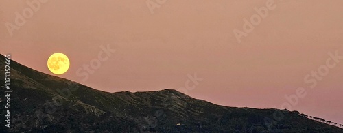 Genova, Italy - January 3, 2026: An amazing photography of the full moon over the city of Genova by night with a great clear and blue sky in the background and some stars.