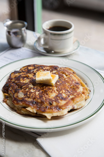 Pancakes with warm maple syrup and butter on a white plate in a restaurant setting.