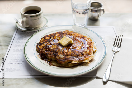 Pancakes with warm maple syrup and butter on a white plate in a restaurant setting.