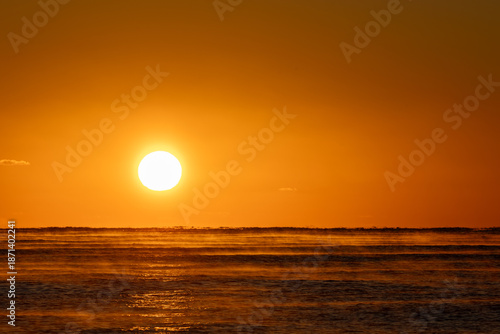 Golden Sunrise Over Calm Ocean With Sea Smoke and Layered Waves