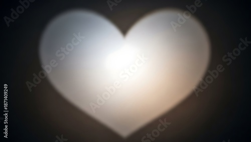 A glowing white heart shape on a dark background is viewed directly, emitting a soft glow.