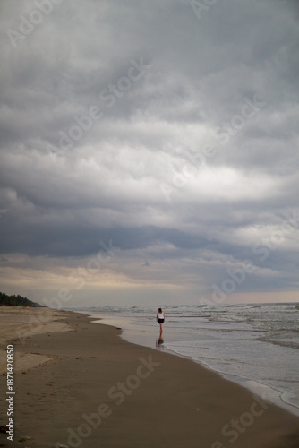 Femme marchant sur la plage d’Assinie (Côte d’Ivoire) avec un ciel menaçant et tourmenté au dessus de sa tête.