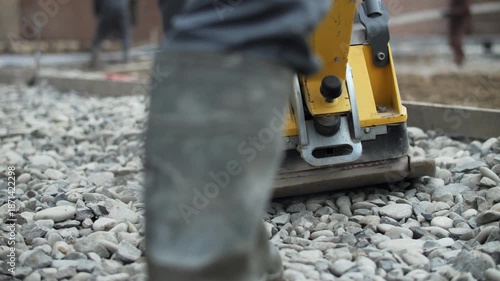 Plate compactor compacting gravel surface at construction site