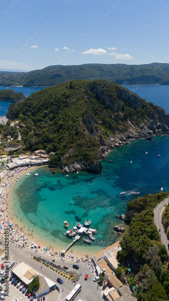 Fototapeta premium Vertical aerial view of crowded beach and turquoise bay in Paleokastritsa, Corfu, Greece