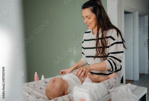 Obraz na plátne Young mother smiling at baby lying down on changing table