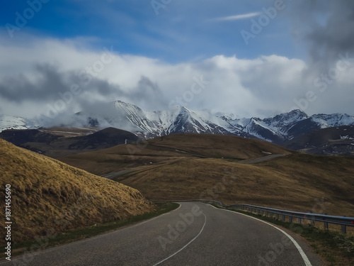 Asphalt road in the Caucasus Mountains with a beautiful view against the backdrop of mountain ranges and cliffs with snow and glaciers on a cloudy, rainy day, landscape for background