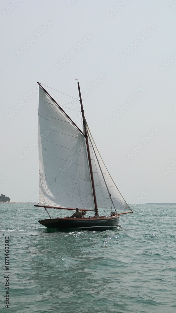Fototapeta premium Voilier traditionnel en bois naviguant sur une mer calme avec voiles blanches