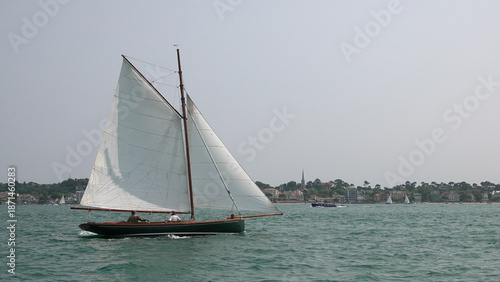 Foto Voilier traditionnel en bois naviguant sur une mer calme avec voiles blanches