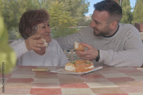 Mother and son enjoying a meal together, dessert, King Cake, and sweets. Happy to be reunited, they eat together at their country home, surrounded by love and affection. A Christmas reunion for mother