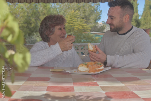 Mother and son enjoying a meal together, dessert, King Cake, and sweets. Happy to be reunited, they eat together at their country home, surrounded by love and affection. A Christmas reunion for mother