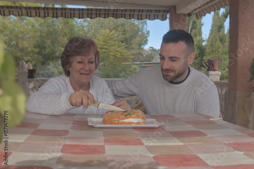 Mother and son enjoying a meal together, dessert, King Cake, and sweets. Happy to be reunited, they eat together at their country home, surrounded by love and affection. A Christmas reunion for mother