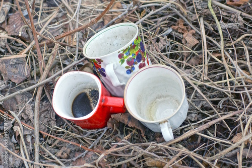 A set of three old ceramic cups stand on the ground in the dry grass on an autumn street