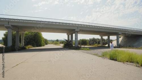 Lone woman in white walking underneath a concrete bridge
