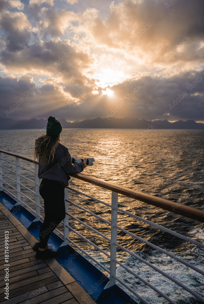 Fototapeta premium Epic Sunset Cruise Ship Female Photographer Looks Over Balcony at Heavenly Sun Beams Through Clouds Over Ocean. Colorful Landscape Dreams Adventure