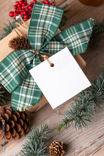 Christmas square paper gift tag mockup on a rustic wooden table with fir tree branches and decorations top view. Rustic winter composition with blank Gift tag Mockup, copy space