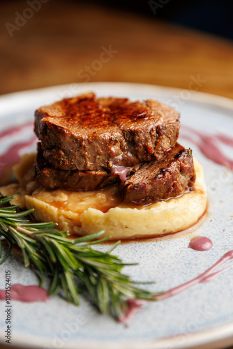 Delicious beef tenderloin served over creamy mashed potatoes with a red wine reduction and a sprig of rosemary on the plate