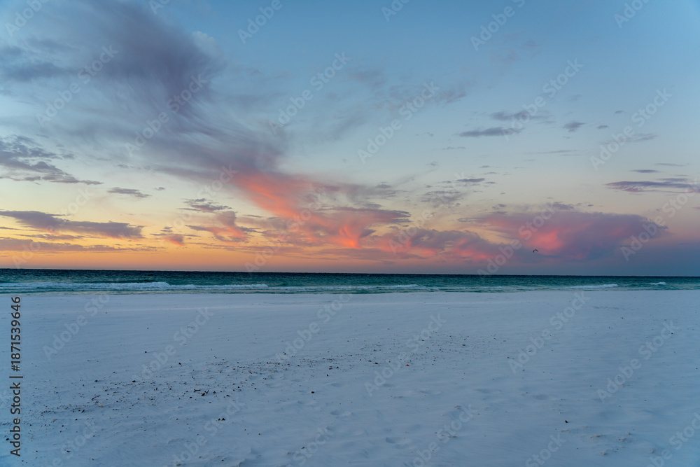 Obraz premium Pink clouds over a beach at sunset with kite surfer.