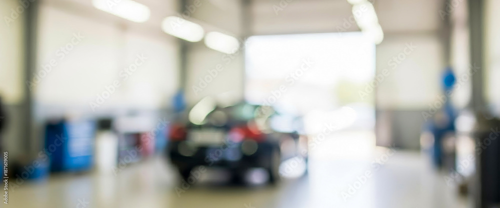 Fototapeta premium Blurred view of a car in an automotive repair shop. Bright overhead lights illuminate the spacious interior filled with equipment for vehicle maintenance and repair.