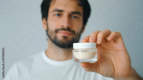 Bearded man presenting a small jar of organic skincare products