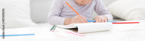 Fotografie 白いリビングで色鉛筆を使い、夢中でお絵かきやぬり絵を楽しむ幼児　想像力や創作力を育む、非認知能力を育てる　顔無しのバナー
