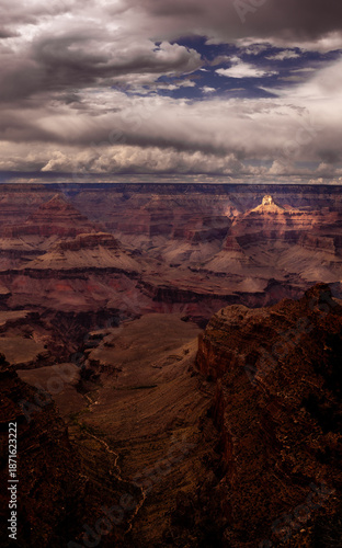Dramatic Vertical Panorama of Grand Canyon with Sunlight Illuminating a Peak Under Stormy Skies