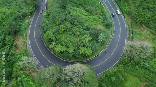 Scenic aerial of a mountain circular roadway surrounded by dense trees, light vehicle flow highlighting a serene and cool environment.