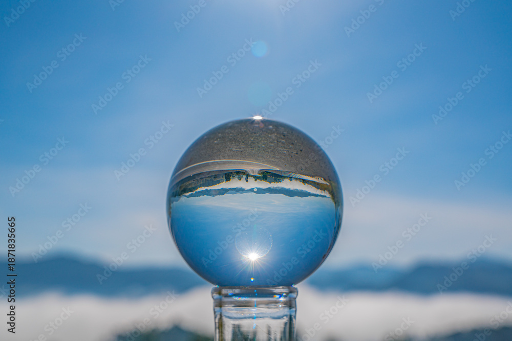 Fototapeta premium A crystal ball on an open road reflects a mist-covered mountain village, revealing a surreal persp Perspective of the Unknown Crystal Ball on a Misty Road ective of a journey into the unknown.