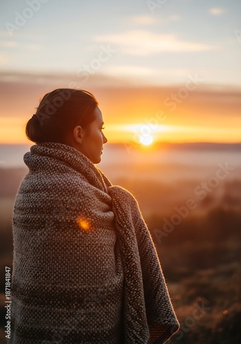 Woman Wrapped in Blanket Watching Sunrise in Serene Landscape.