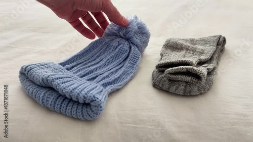 A blue knitted beanie with pom-pom and folded gray socks rest on a soft surface, showcasing cozy winter accessories, textured fabric, and a simple seasonal setup