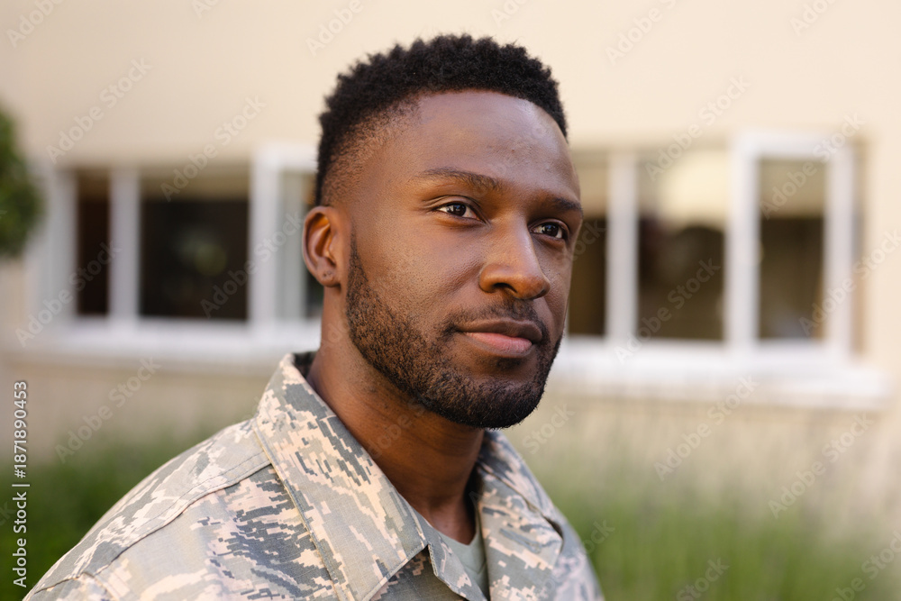 Fototapeta premium Thoughtful african american army soldier with beard looking away against house