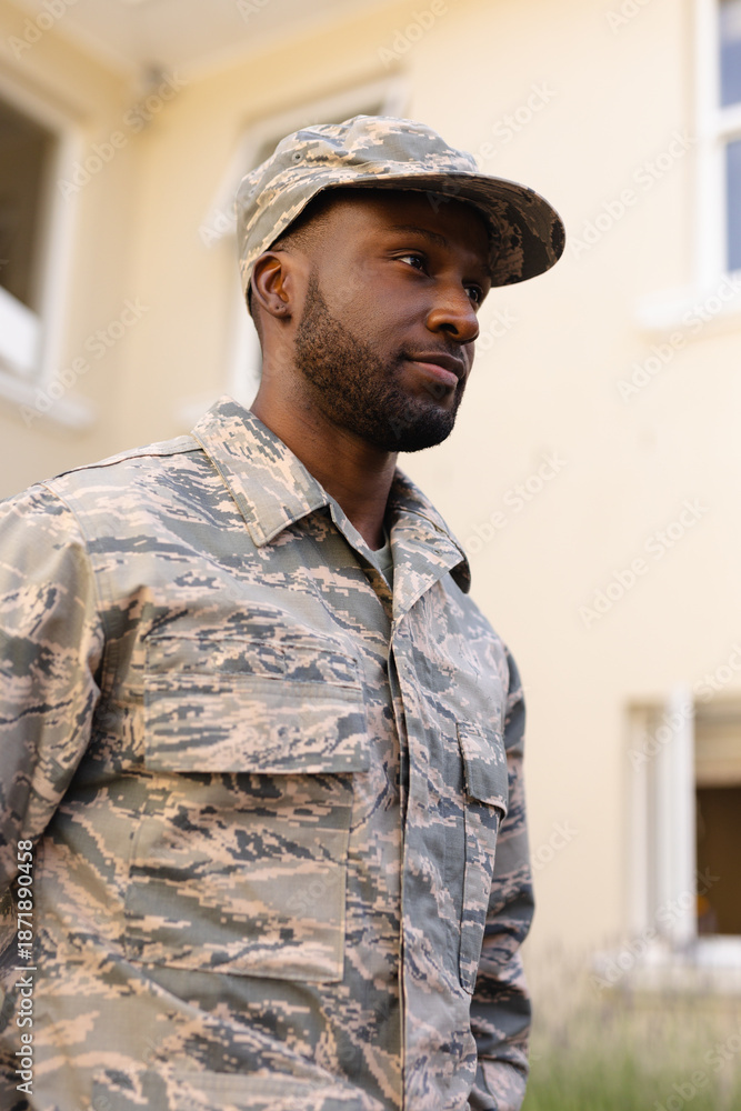 Fototapeta premium African american army man wearing camouflage uniform and cap looking away against house