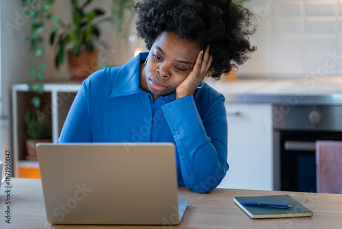 Photos Tired disinterested black woman unmotivated looking at laptop with weary eyes in kitchen