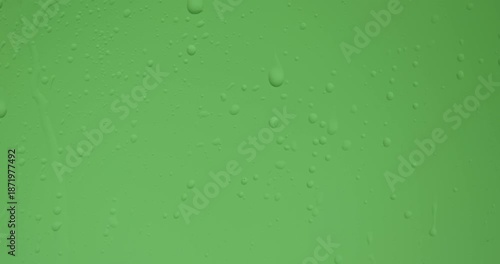 Close up of wet glass with dripping water drops and streaks of rain, on a bright green chroma key background, perfect for visual effects and background replacement. Slow motion.
