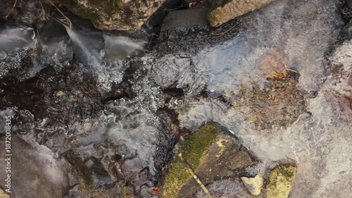 Icy waters flow under the ice in a small mountain stream