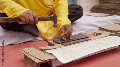 Indian artisan punching Jacquard cards by hand using hammer and tool to create weaving patterns for traditional silk sarees like Banarasi and Kanchipuram. Close-up of craft process.