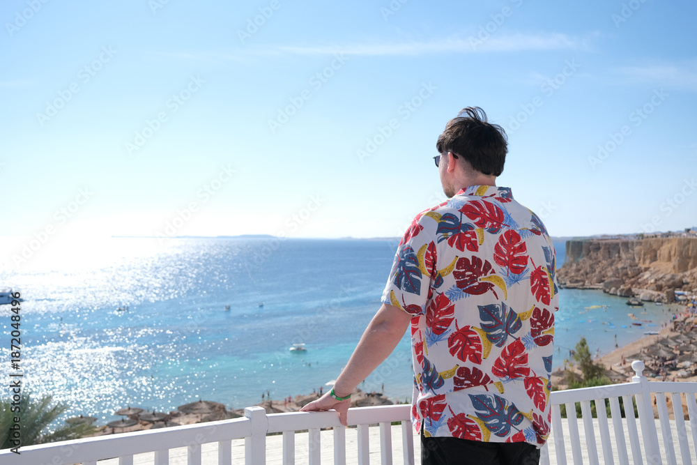 Fototapeta premium young man in Hawaiian shirt standing on terrace overlooking red sea, Egypt