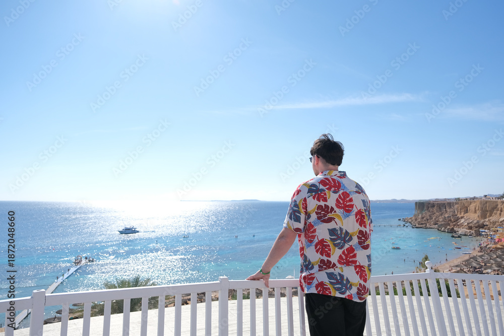 Fototapeta premium young man in Hawaiian shirt standing on terrace overlooking red sea, Egypt