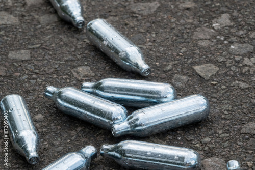 Discarded nitrous oxide gas cartridges on asphalt ground, pollution and waste concept