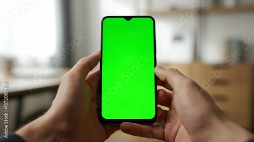 First person perspective of a man holding a smartphone with a green screen display.