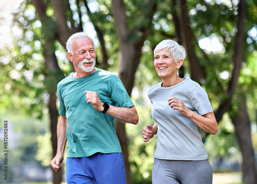 Fototapeta premium Smiling active mature senior couple jogging together in the park
