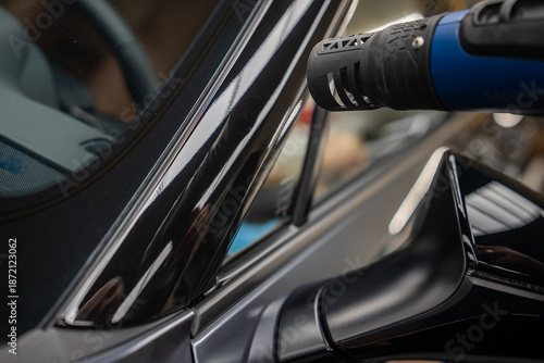 Canvas Print A technician uses a heat gun to shrink glossy black vinyl on the B pillar and mirror of a luxury car in a dealer workshop, with reflections and controlled indoor lighting