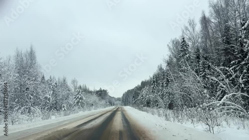 Front view driving plate on empty snowy road curving through snow covered forest under overcast sky