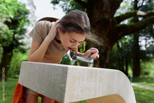 Obraz na plátně Girl drinking water from outdoor fountain in park, child leaning over concrete b