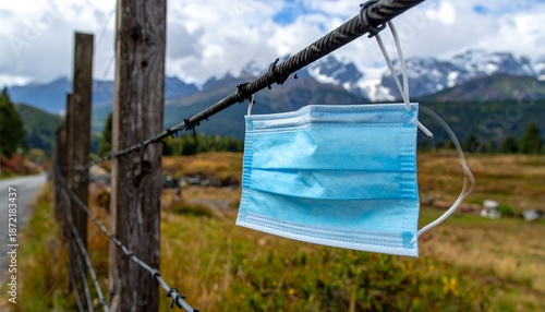 Disposable Face Mask Hanging on Barbed Wire Fence in Scenic Mountain Landscape