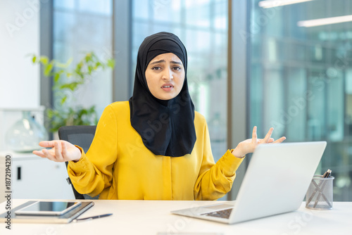 Φωτογραφία Muslim businesswoman wearing a hijab expressing doubt and frustration while shru